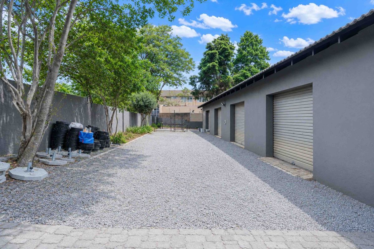 A spacious rear exterior area featuring a gravel driveway, perimeter wall, and multiple roller shutter garage doors.
