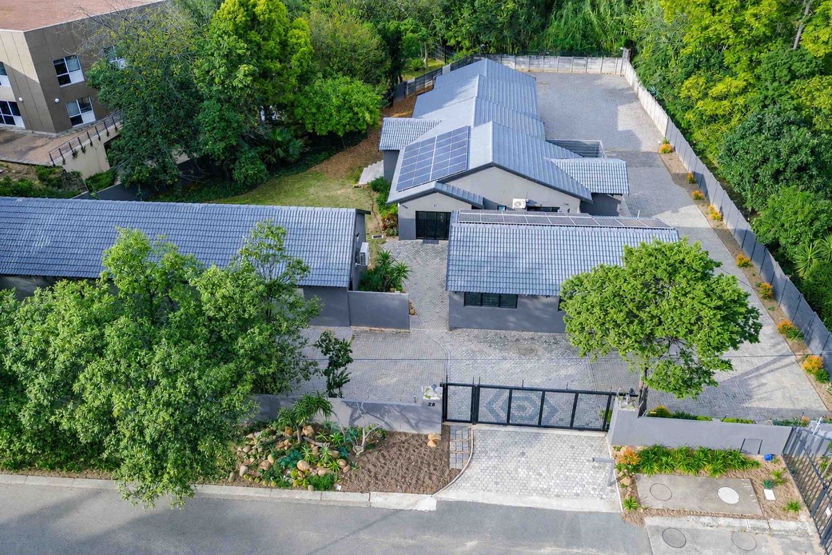 Aerial view of a residential property featuring a paved driveway, secure gated entrance, solar panels, and established garden surroundings.
