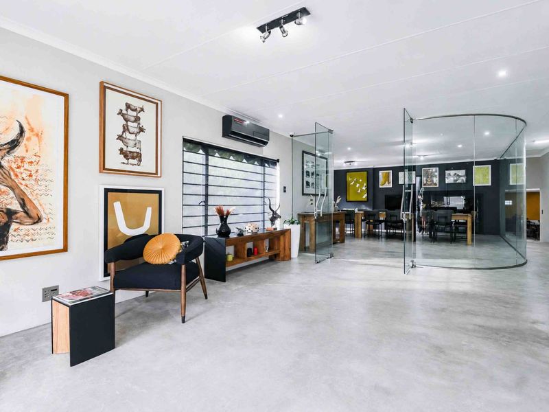 Spacious open-plan living area featuring polished concrete floors, modern track lighting, and a distinctive curved glass partition wall creating a versatile interior space.