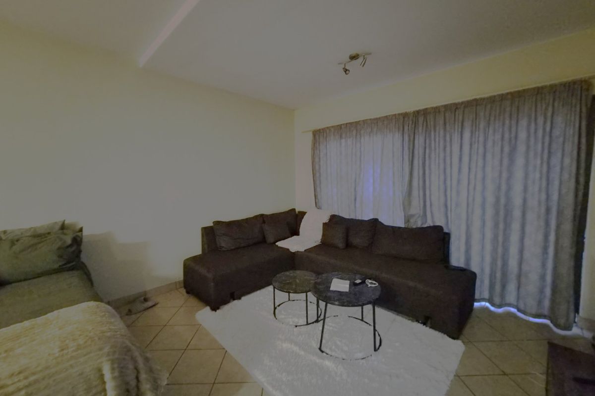 A living room area featuring tiled flooring and a recessed ceiling detail, providing a functional space for relaxation.