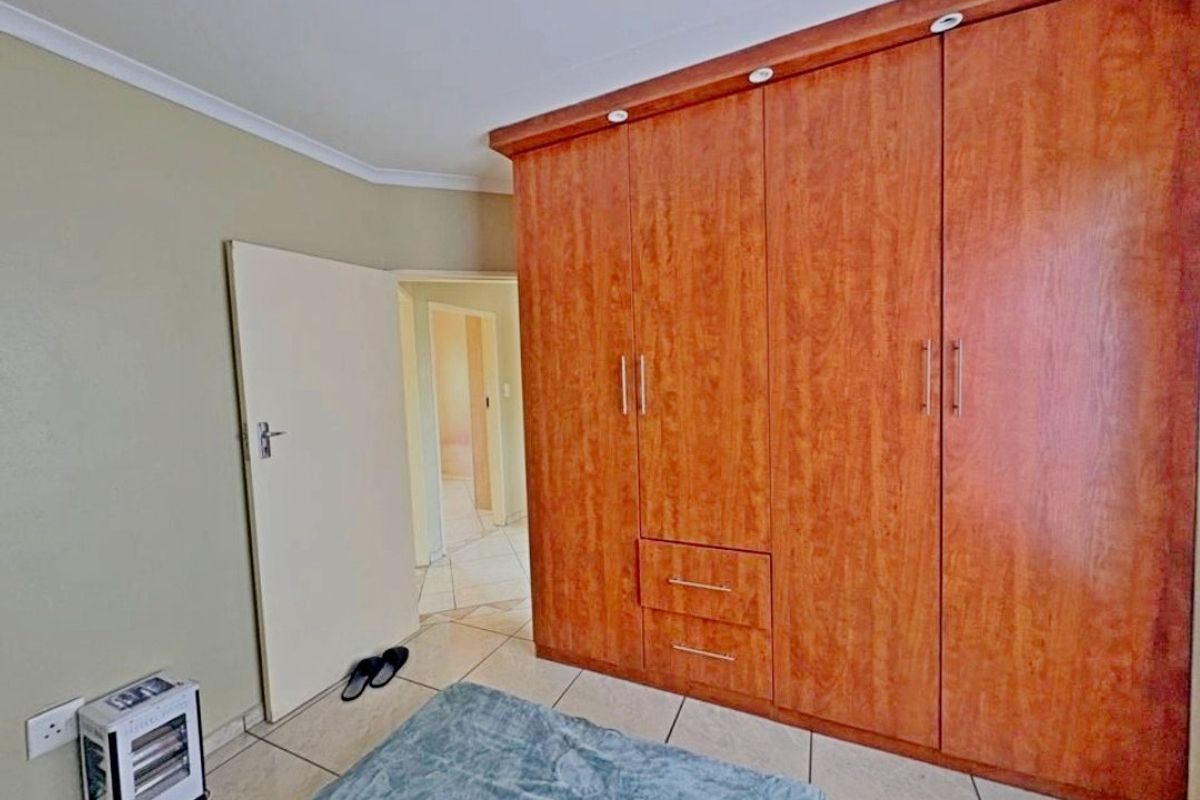 A bedroom featuring built-in wooden cupboards, tiled flooring, and a coved ceiling, providing functional storage and a neutral base.