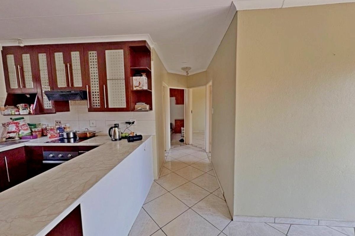 A functional kitchen featuring dark wood cabinetry, a breakfast bar, and tiled flooring, leading into a hallway with access to other rooms.