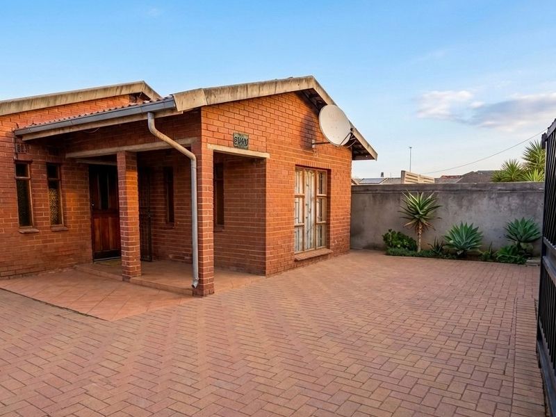 A well-maintained face brick house featuring a paved driveway, covered entrance porch, and secure boundary walling.
