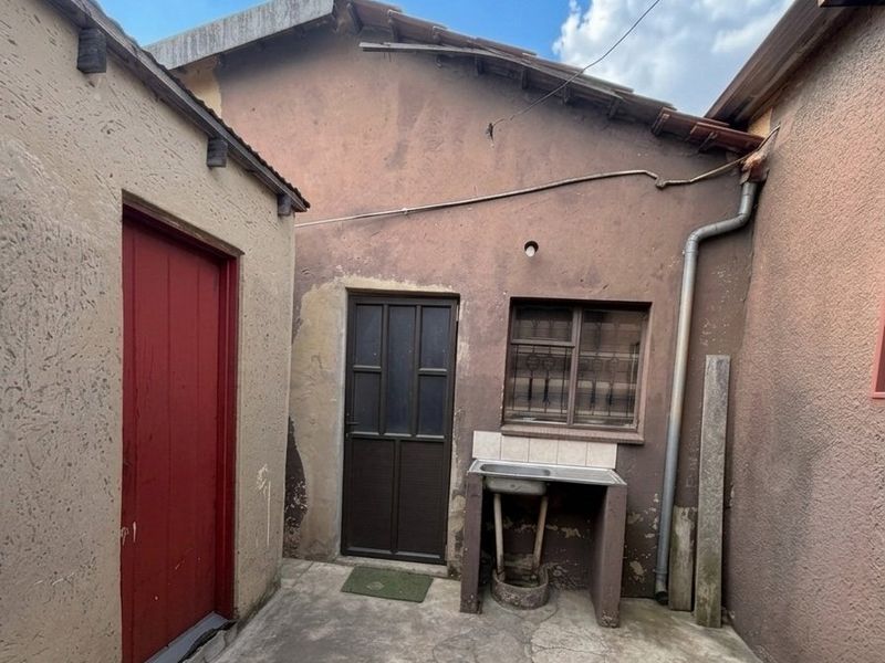 A rear courtyard area featuring a concrete wash basin, weathered exterior walls, and cracked concrete flooring, showing significant signs of wear and maintenance requirements.
