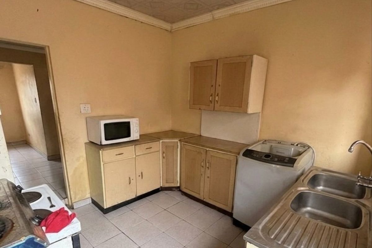A dated kitchen featuring built-in cabinetry, a double bowl stainless steel sink, and tiled flooring, offering significant potential for renovation and modernization.