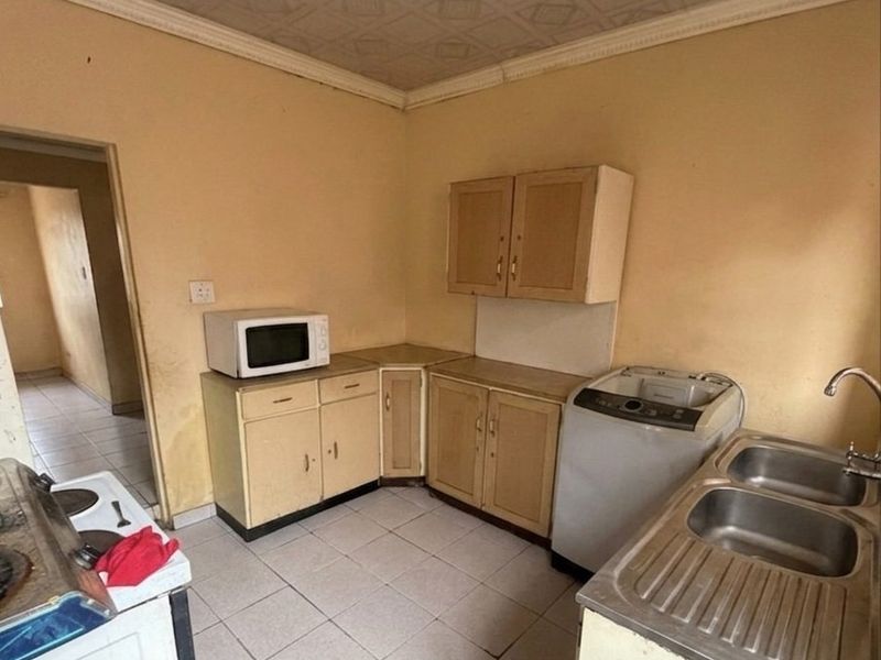 A dated kitchen featuring built-in cabinetry, a double bowl stainless steel sink, and tiled flooring, offering significant potential for renovation and modernization.