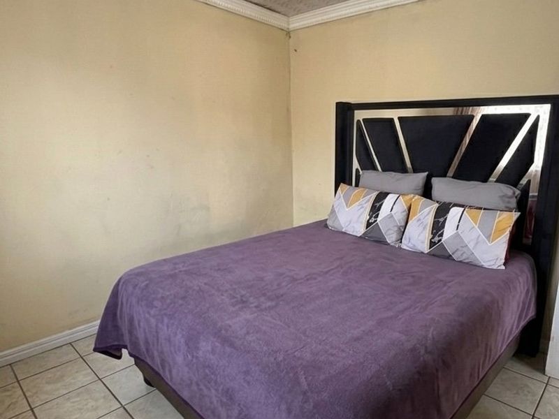 A bedroom featuring tiled flooring and a textured ceiling with cornice detailing. The walls show signs of wear and require cosmetic attention.