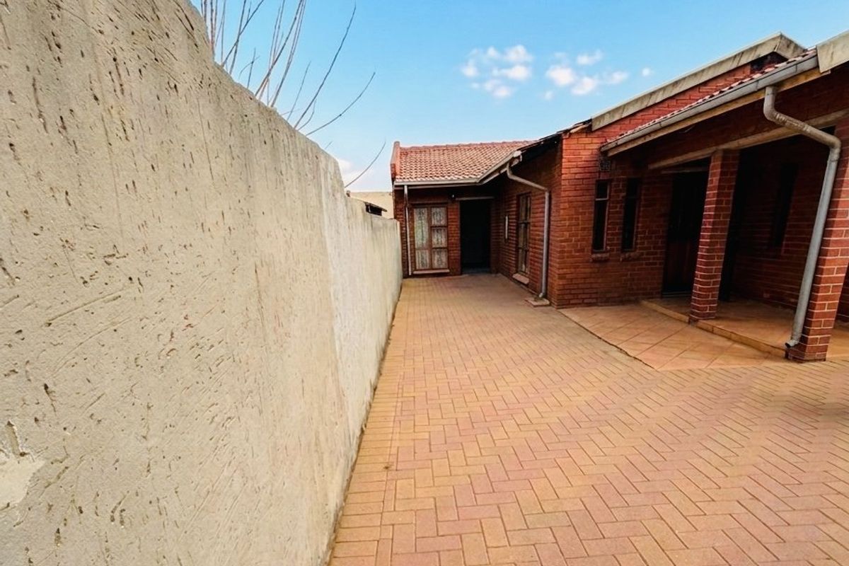 A side view of the property featuring brick paving, a tiled roof, and a high boundary wall.
