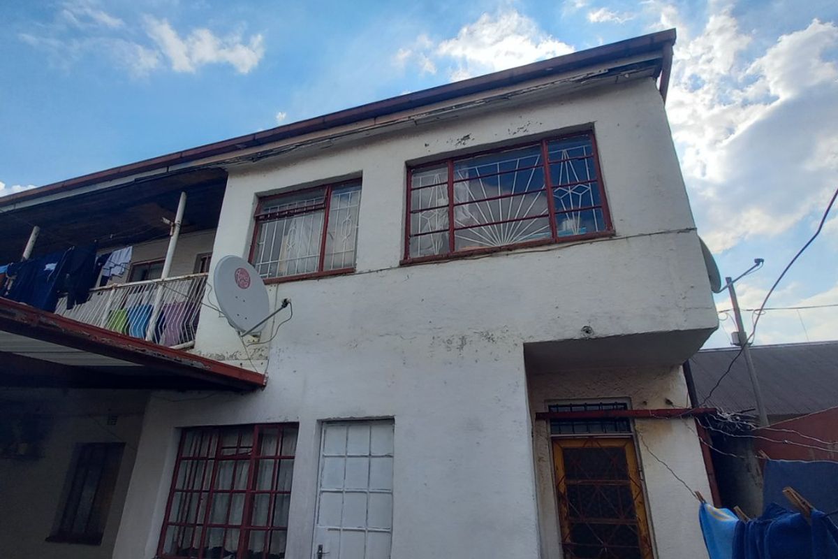 Rear elevation of a two-story house featuring a balcony, metal security bars on windows, and visible exterior wall maintenance requirements.