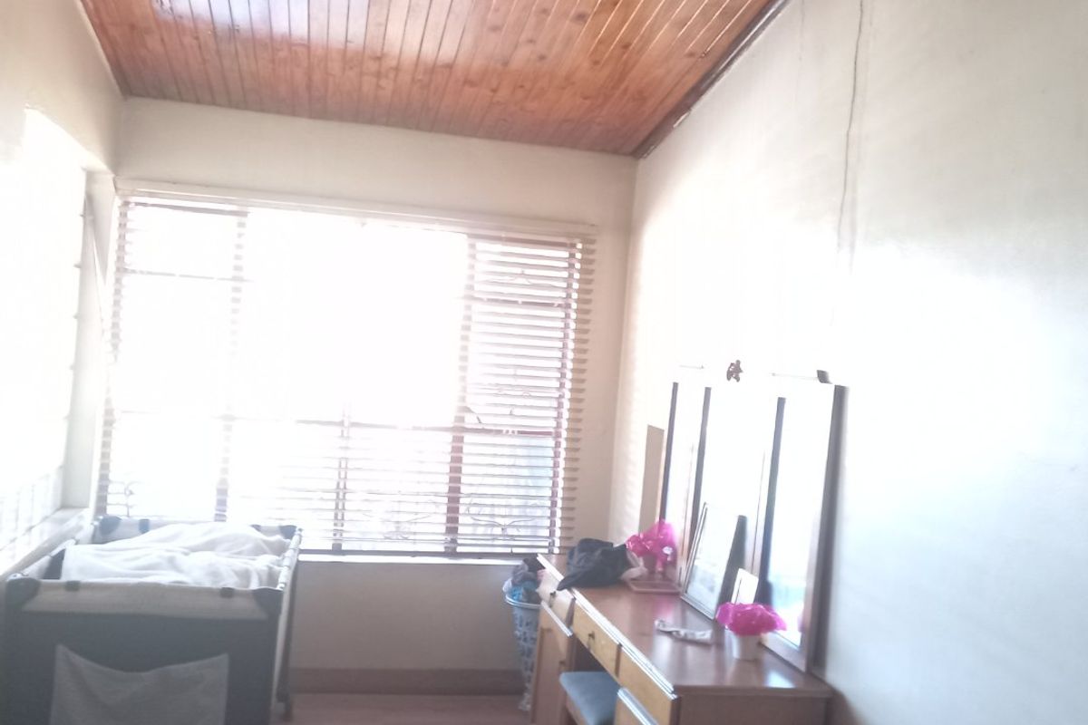 A bedroom featuring a timber tongue and groove ceiling, laminate flooring, and large windows with venetian blinds.
