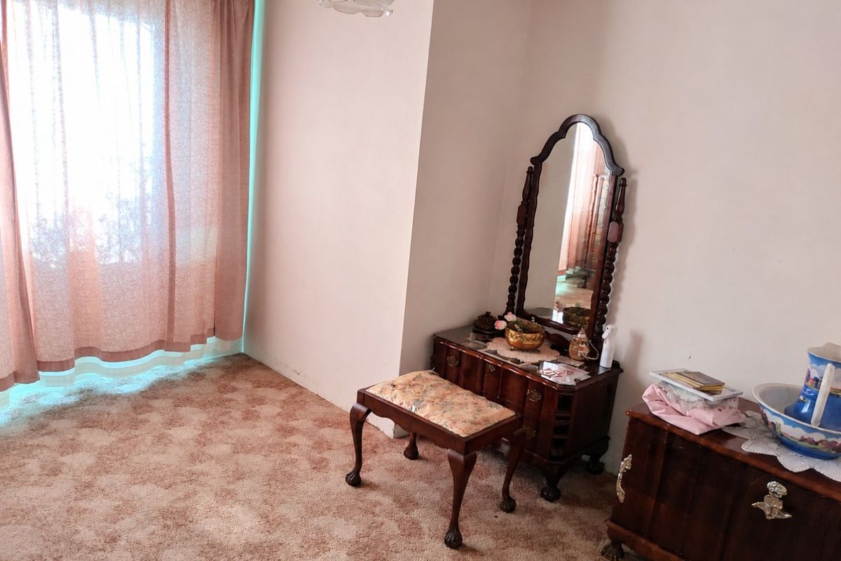 A bedroom featuring carpeted flooring and natural light through window curtains, presenting an opportunity for modernization and cosmetic updates.