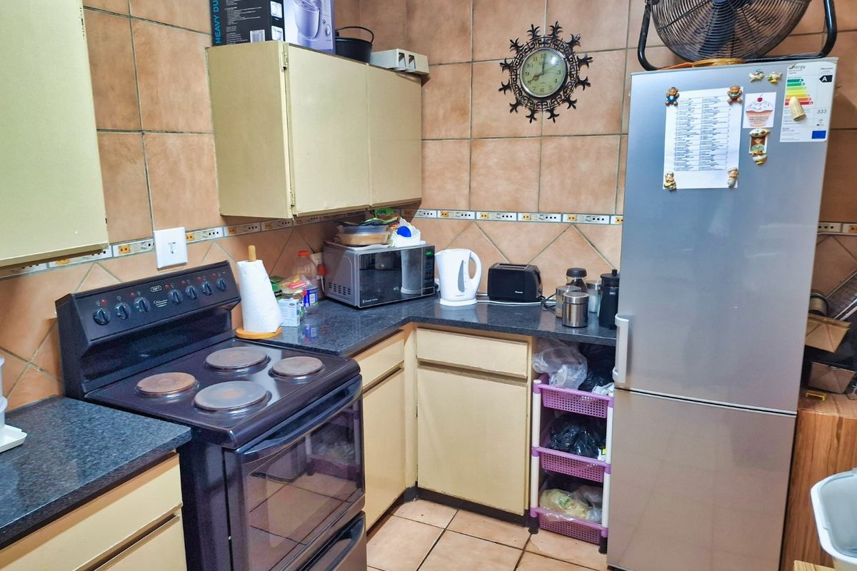 A compact kitchen featuring dated cabinetry, ceramic wall tiling, and a freestanding electric stove, offering potential for a modern renovation.
