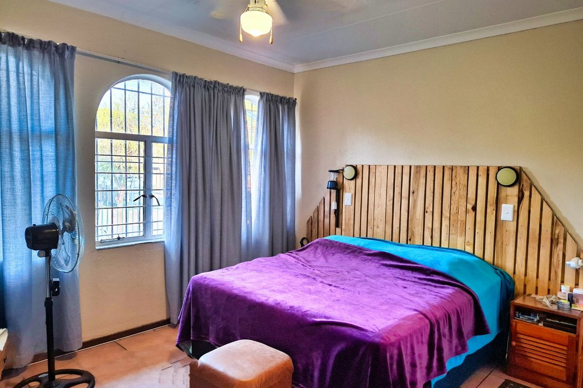 A bedroom featuring tiled flooring, an arched window with security bars, and a ceiling fan.