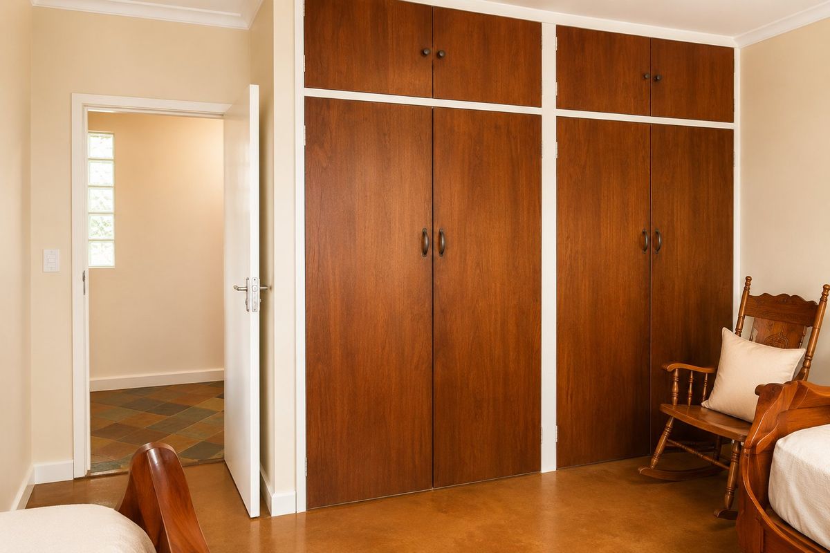 A bedroom featuring built-in wooden cupboards with overhead storage and a glass block window, providing access to an adjacent tiled room.