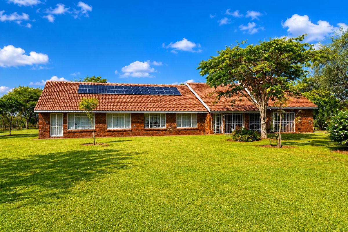 Rear view of a well-maintained facebrick farmhouse featuring a tiled roof with integrated solar panels and a spacious surrounding lawn.