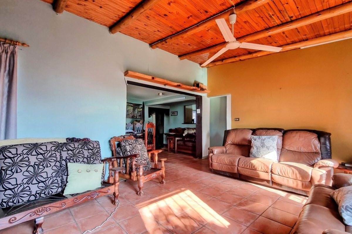 Spacious living room featuring a rustic exposed timber beam ceiling, ceiling fan, and terracotta floor tiles, with an open transition to the adjacent room.