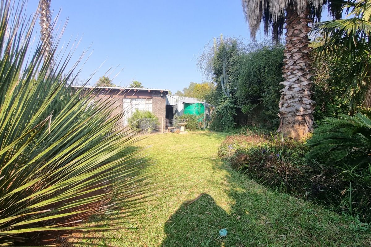 A view of the rear garden featuring a brick exterior wall, established trees, and a water tank.