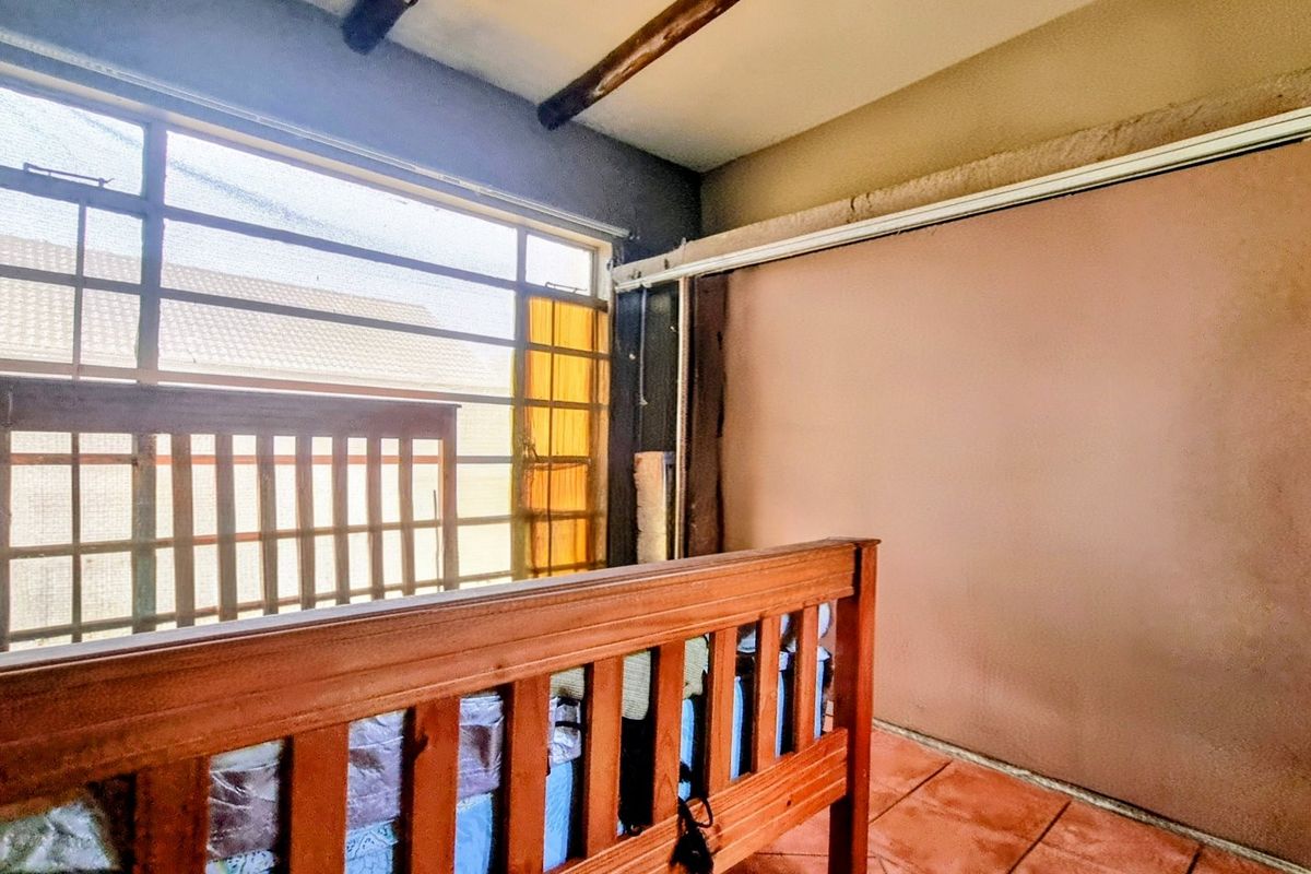 A bedroom featuring exposed timber ceiling beams, large steel-framed windows, and tiled flooring, currently requiring cosmetic updates to the wall finishes.