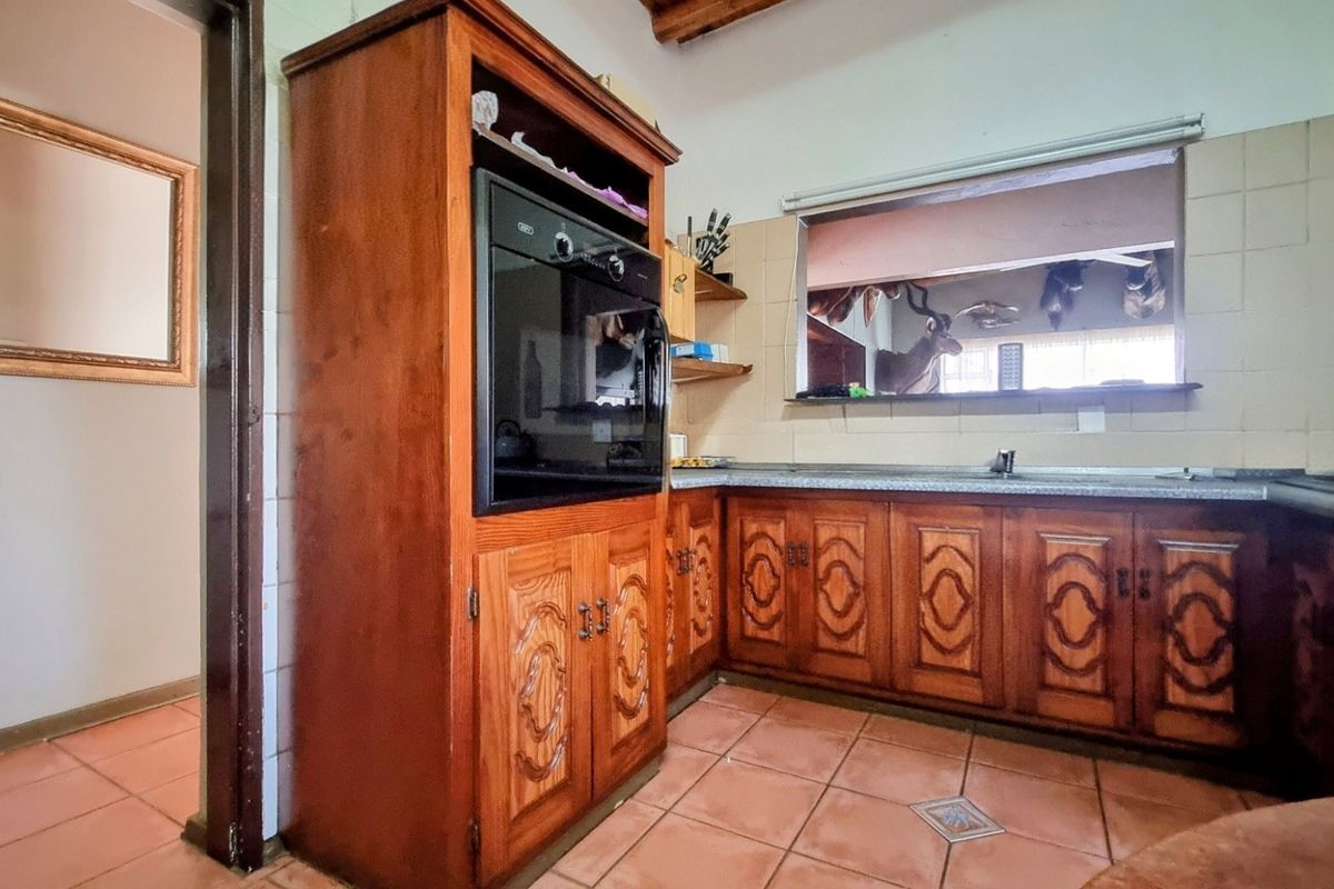 A dated kitchen featuring traditional wooden cabinetry, built-in oven, tiled flooring, and a convenient pass-through window connecting to the adjacent living space.