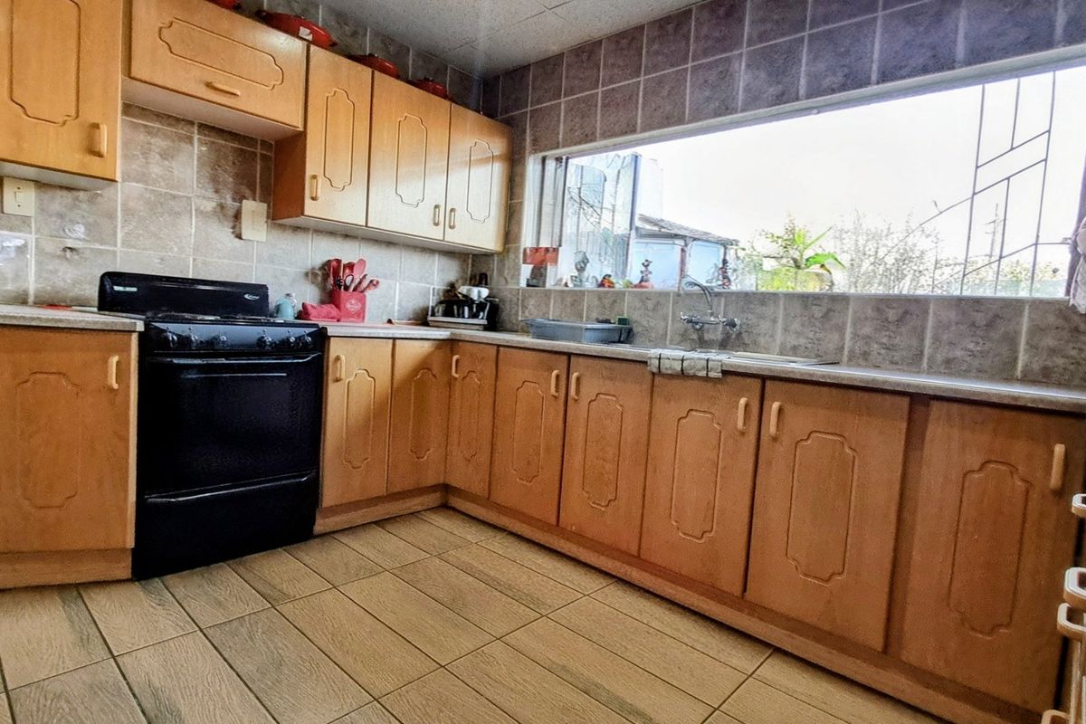 A functional kitchen featuring wooden cabinetry, tiled backsplash, tiled flooring, and a large window providing natural light.