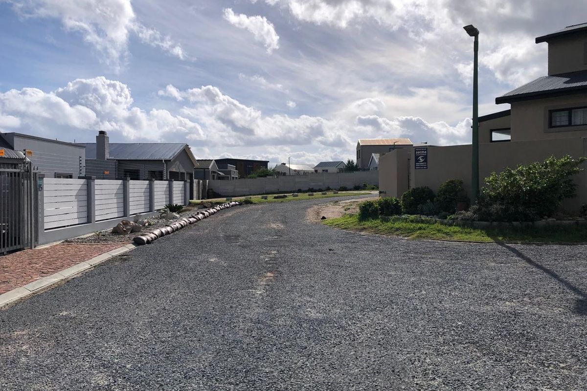 A view of a gravel residential street with perimeter walls and street lighting in a developed estate setting.