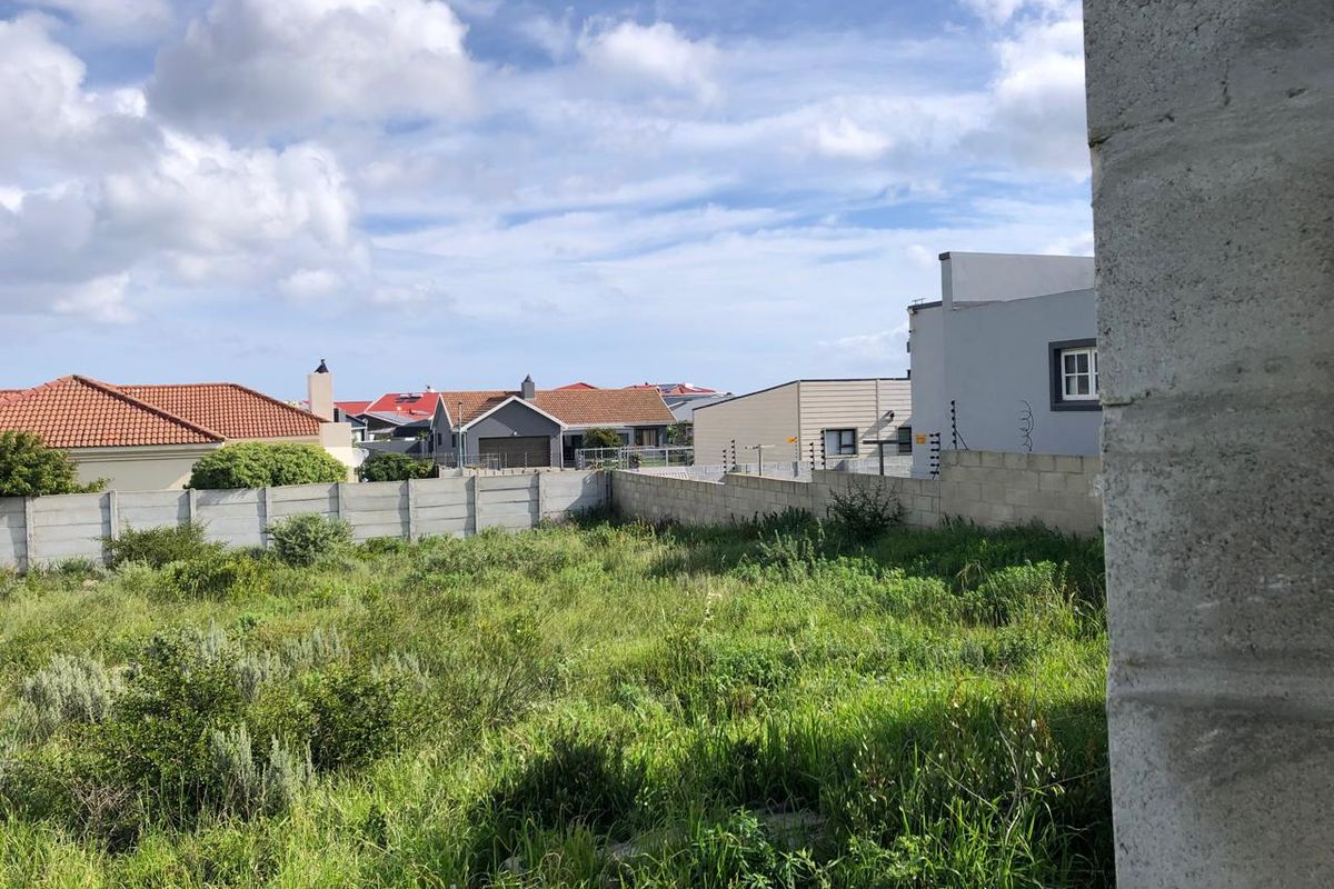 A vacant residential plot featuring overgrown grass, enclosed by a precast concrete boundary wall with installed electric fencing.