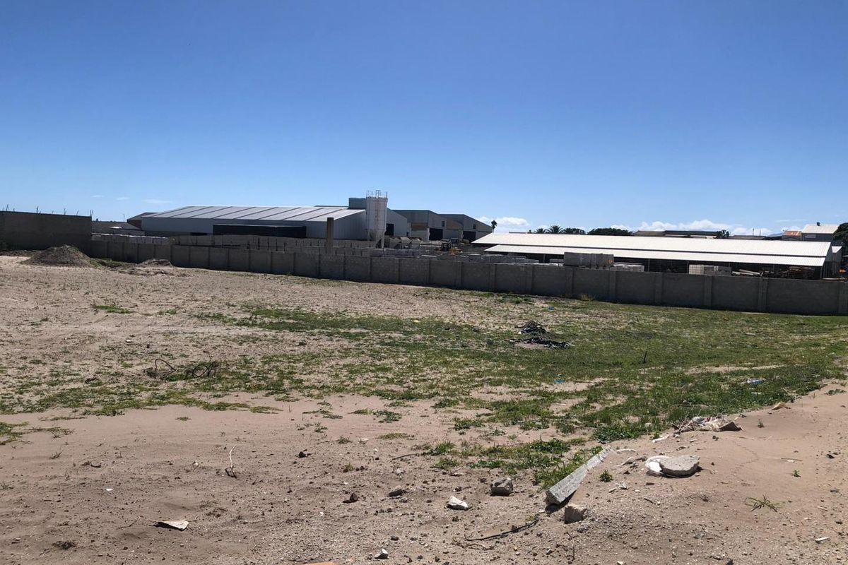 Expansive vacant industrial land plot featuring a perimeter wall and views of adjacent warehouse facilities.