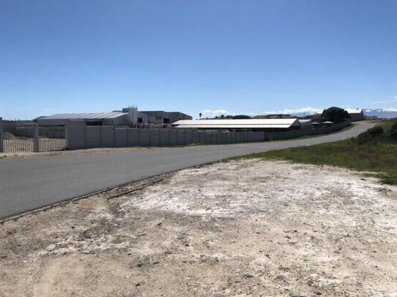 Street view of an industrial property featuring a perimeter wall, metal gate access, and warehouse structures under a clear sky.