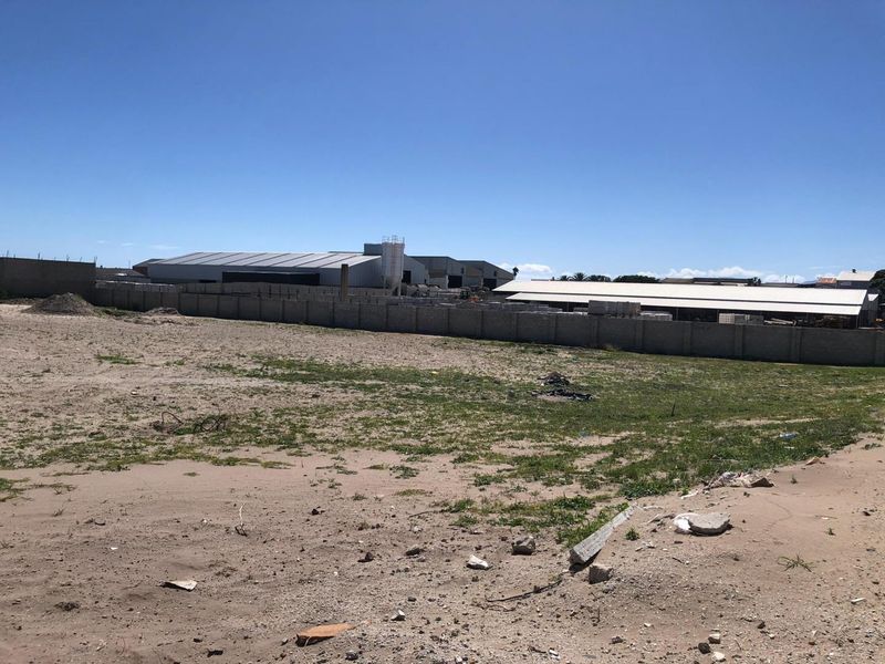 Expansive vacant industrial land plot featuring a perimeter wall and views of adjacent warehouse facilities.