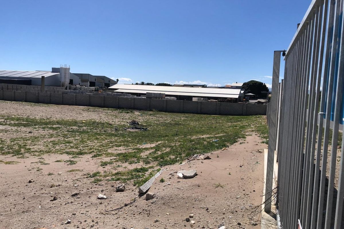 An expansive, unimproved industrial plot enclosed by a perimeter concrete wall and metal security fencing.