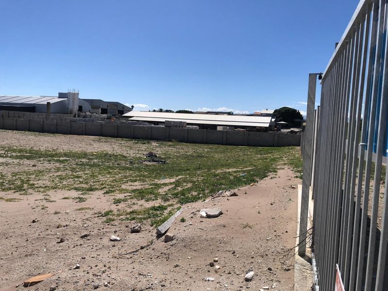 An expansive, unimproved industrial plot enclosed by a perimeter concrete wall and metal security fencing.