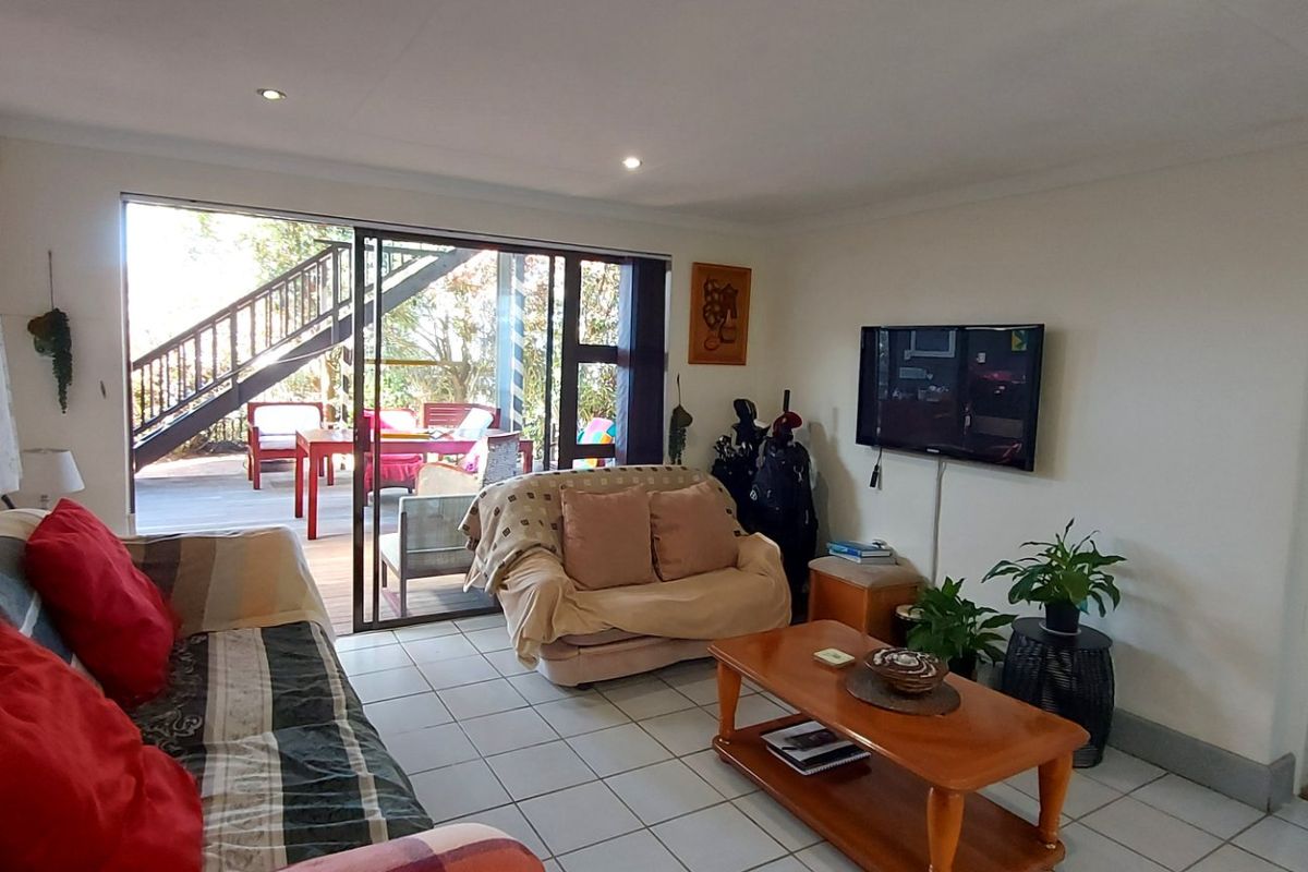 A bright living room featuring tiled flooring, recessed downlighting, and large sliding glass doors providing direct access to an outdoor deck area.