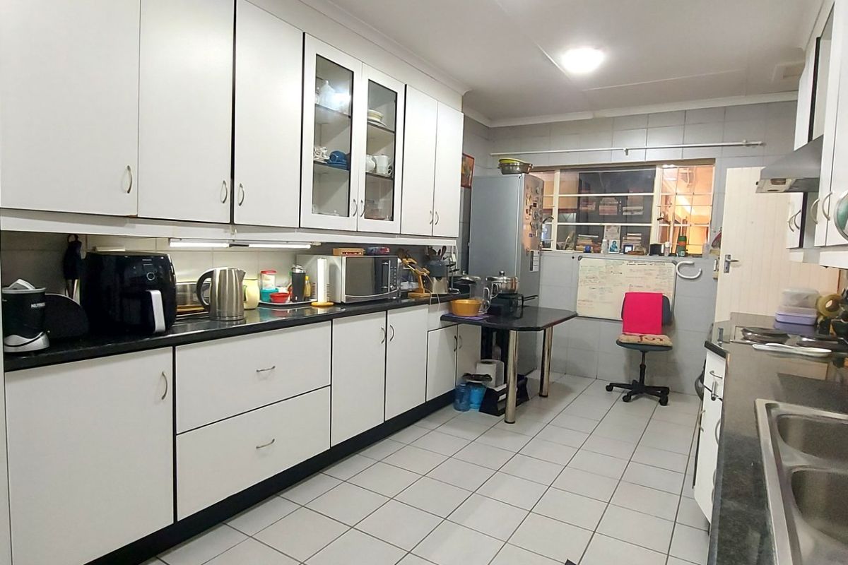 Functional kitchen featuring ample built-in cabinetry, tiled flooring, a double bowl sink, and a tiled backsplash, offering a practical layout for daily use.