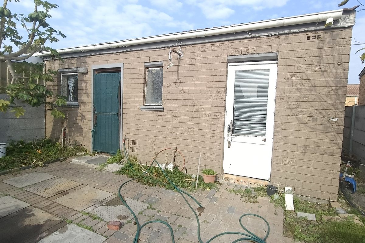 Rear exterior view of a brick-built structure featuring a paved patio area, external doors, and windows requiring maintenance and exterior refurbishment.