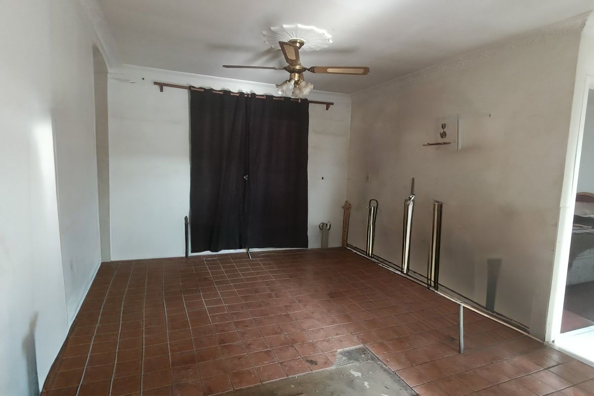 An empty living room featuring tiled flooring, a ceiling fan with a decorative rose, and cornice detailing, requiring cosmetic updates to the wall finishes.