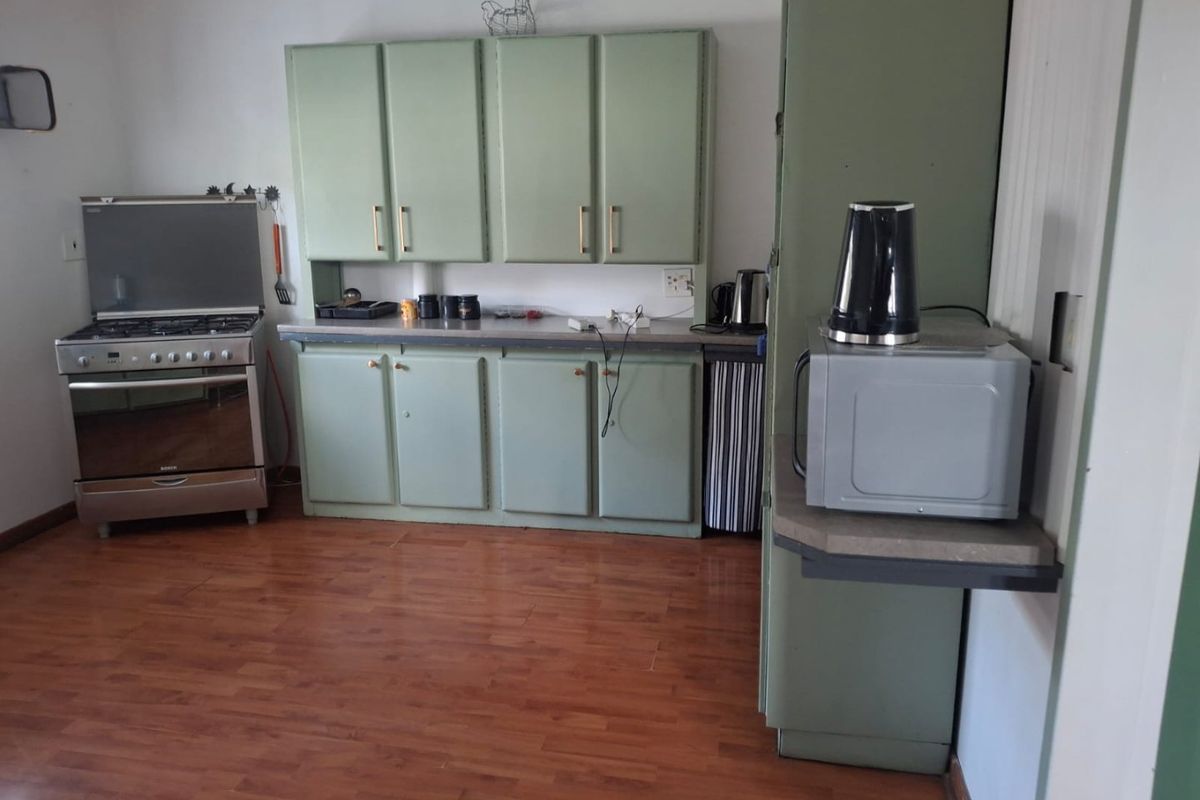 A functional kitchen featuring dated green cabinetry, a gas stove with oven, and laminate flooring, offering potential for a modern renovation.