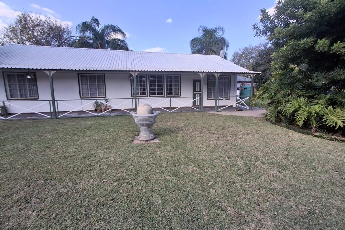 A well-maintained rear exterior view featuring a covered veranda with timber balustrades, a corrugated metal roof, and a landscaped garden with a stone fountain.