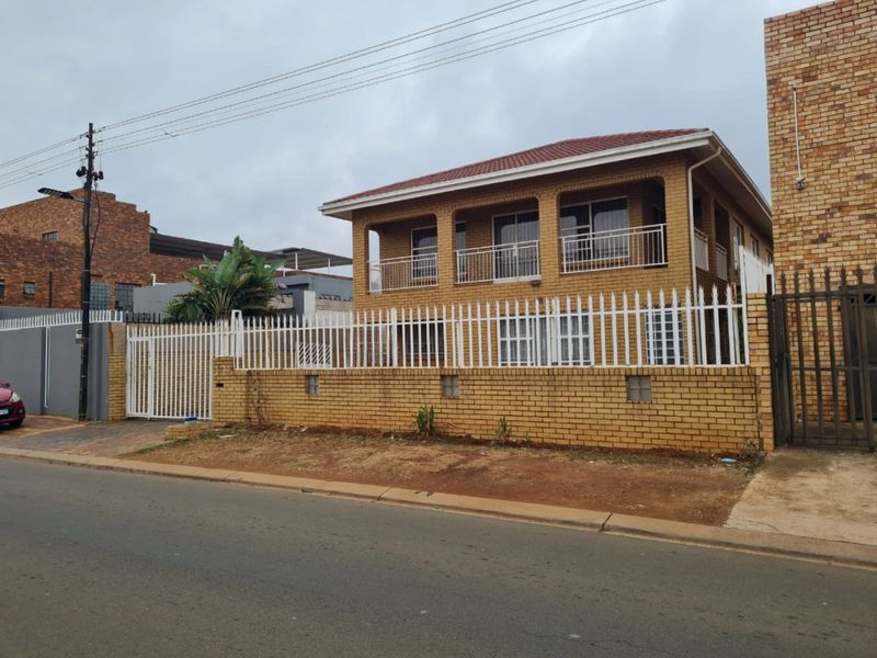 A two-story face brick house featuring a balcony, secure perimeter walling, and metal fencing, viewed from the street.