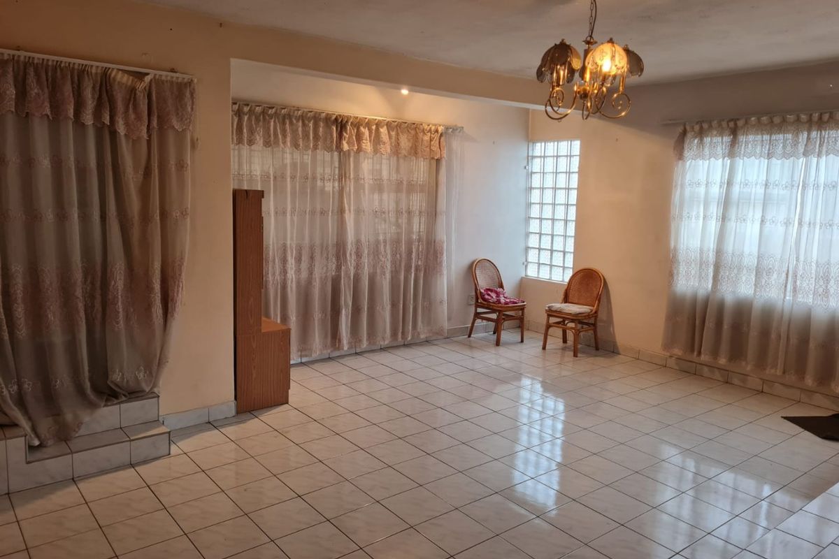 Spacious living area featuring tiled flooring, a decorative chandelier, and a glass block window, offering a blank canvas for renovation and interior design.