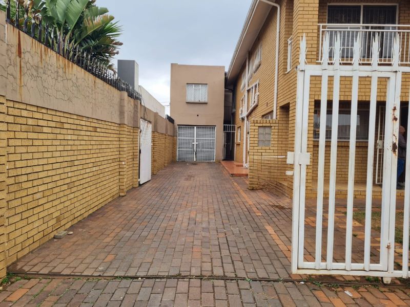 A view of the property entrance featuring a brick-paved driveway, facebrick facade, and secure boundary wall with metal security gates.