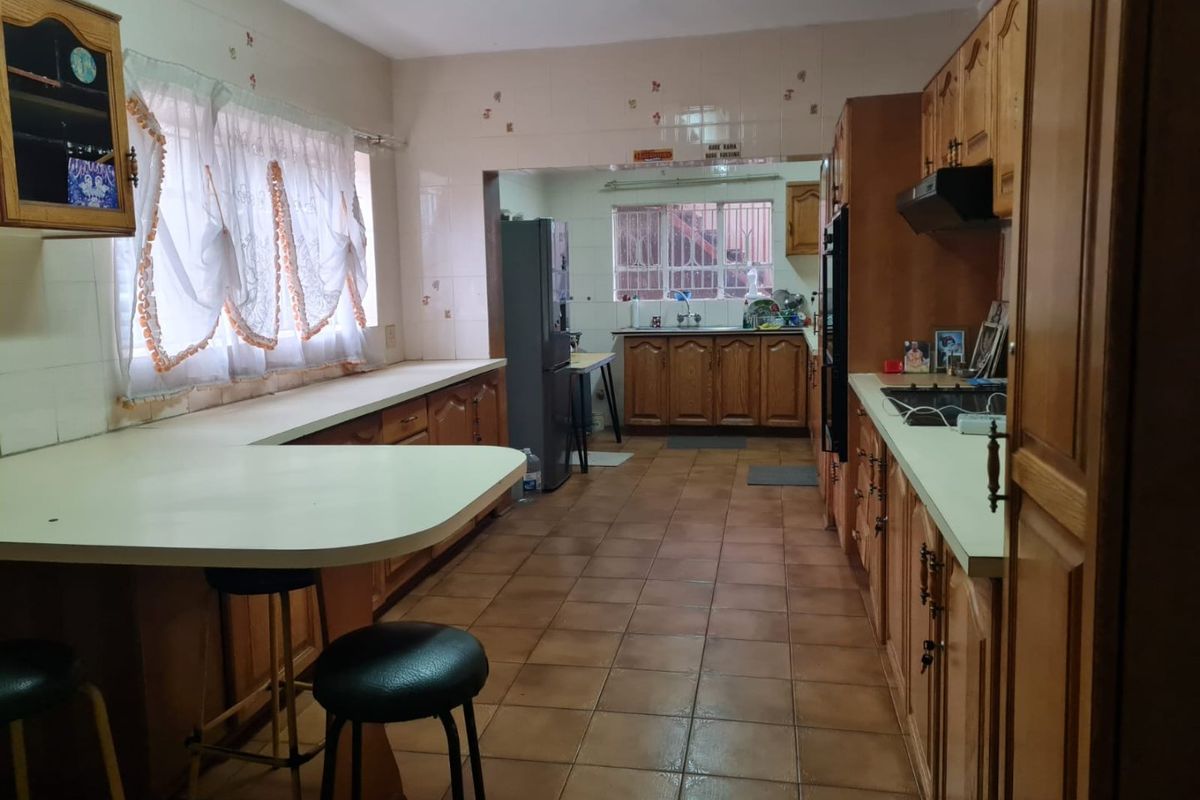 A spacious kitchen featuring traditional wooden cabinetry, tiled flooring, and a functional layout with a breakfast bar and integrated cooking appliances.