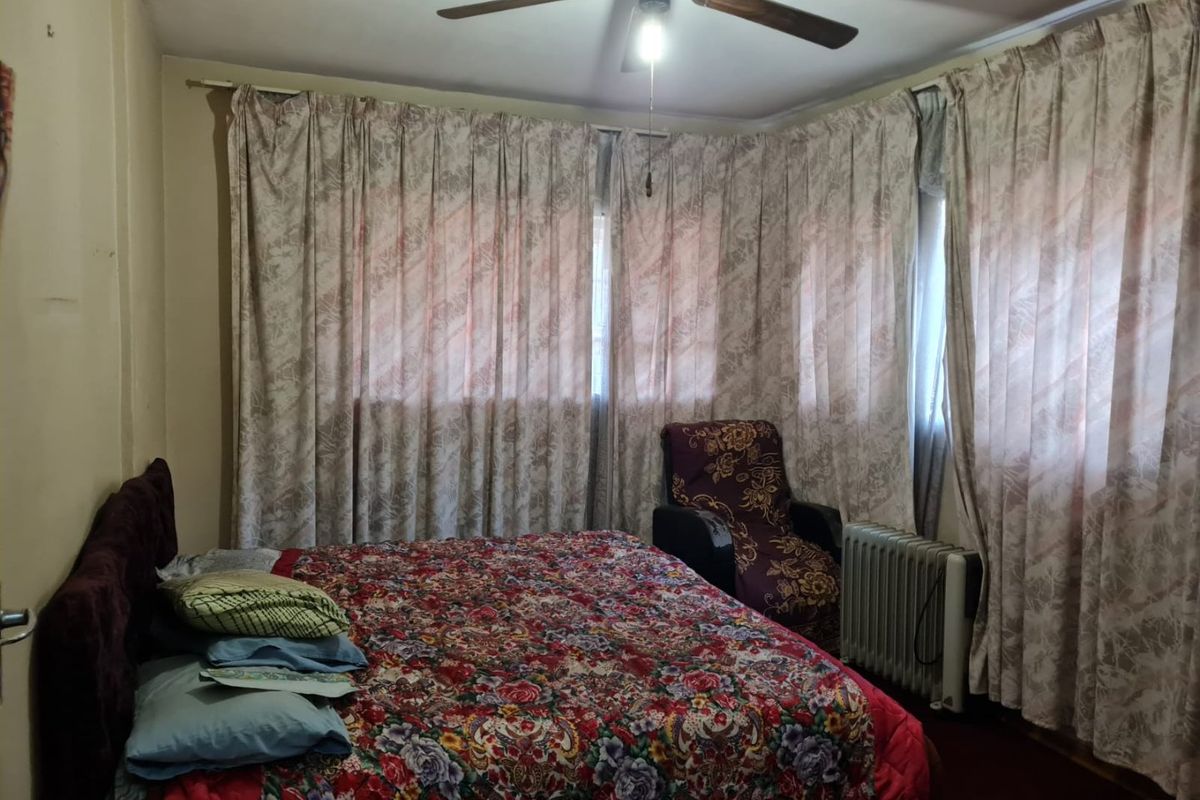 A bedroom featuring a ceiling fan and large windows covered by curtains, offering a functional space with potential for cosmetic updates.