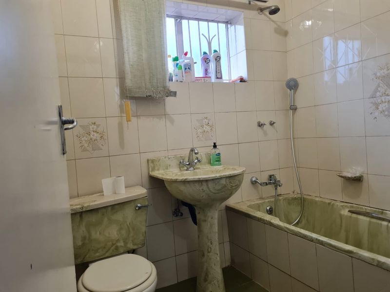 A dated bathroom featuring a pedestal basin, bathtub with handheld shower mixer, and toilet, finished with ceramic wall tiles.