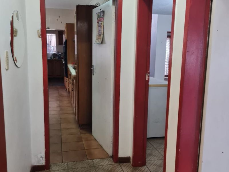 A functional hallway with tiled flooring and red-painted door frames, providing access to the kitchen and adjacent rooms.