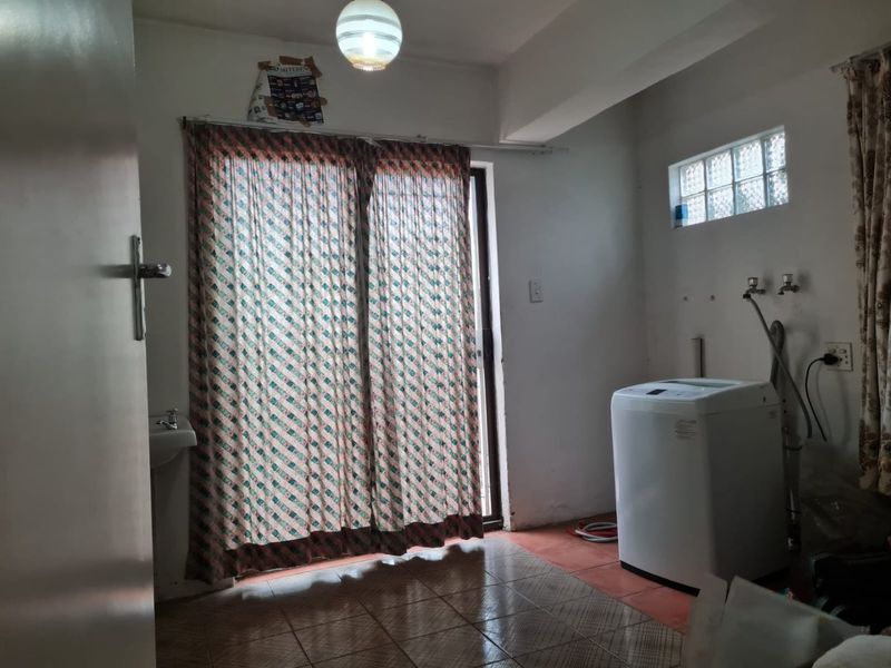 A functional laundry area featuring tiled flooring, plumbing connections for appliances, and a sliding door providing access to the exterior.
