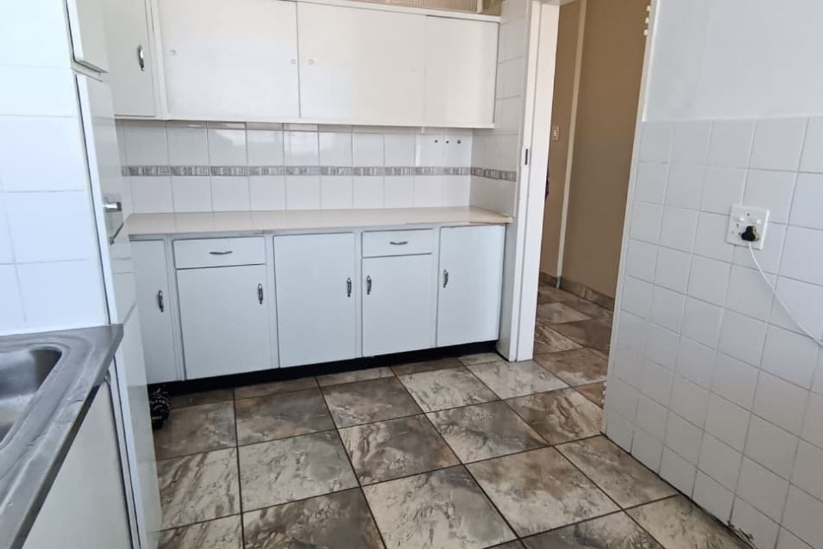 A dated kitchen featuring built-in white cabinetry, tiled splashbacks, and patterned floor tiles, offering a blank canvas for potential renovation and modernization.