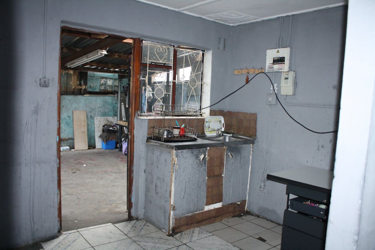 A basic kitchen area featuring a stainless steel sink, tiled flooring, and visible electrical infrastructure, requiring significant renovation and cosmetic updates.
