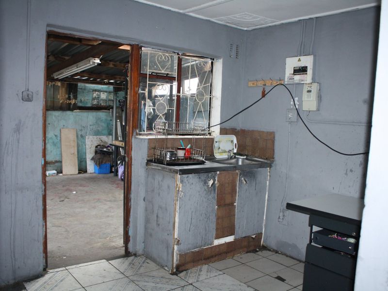 A basic kitchen area featuring a stainless steel sink, tiled flooring, and visible electrical infrastructure, requiring significant renovation and cosmetic updates.