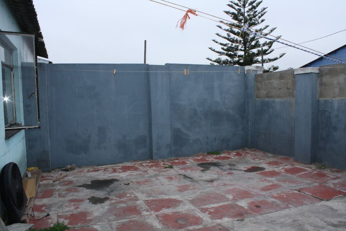 A rear outdoor area featuring a paved patio and high boundary walls, providing a private space for potential landscaping or outdoor improvements.