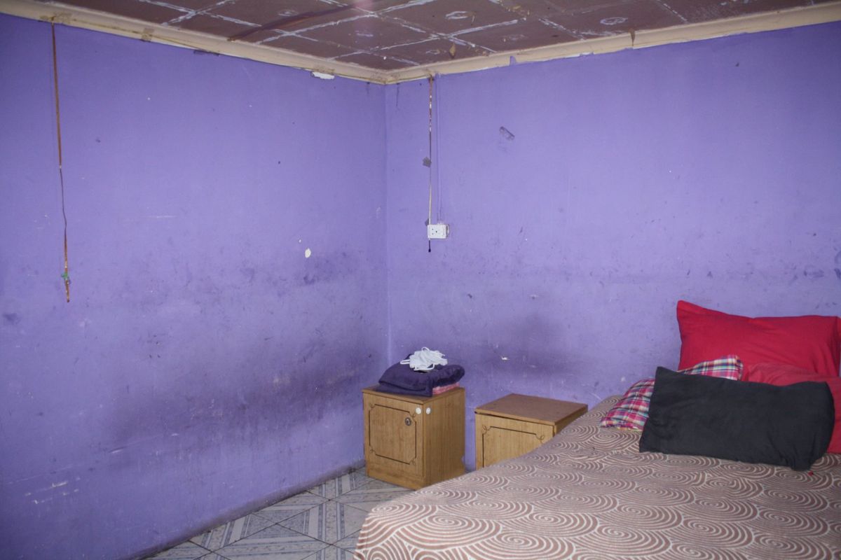 A bedroom featuring tiled flooring and a tiled ceiling, currently requiring significant cosmetic updates and wall repairs.